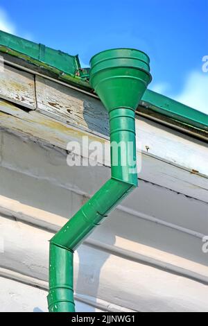 Grüne Drainpipe aka Dach Drainpipe mit Anti-Korrosion-Beschichtung auf vintage weiße Wand mit blauen Himmel und Wolken, Umwelt Vielfalt Stockfoto