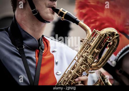 Männlicher Marschkapelle-Musiker in Uniform spielt Trompete - Nahaufnahme und abgeschnitten - Hutband unter dem Kinn Stockfoto