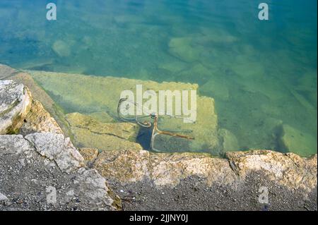 Rostiger Metallstuhl, der in einem alten Steinbruch mit Wasser gefüllt liegt Stockfoto