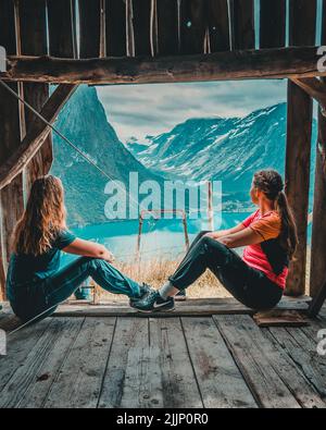 Vertikale Aufnahme von zwei Mädchen sitzen in einem Holzhaus und blicken auf eine atemberaubende Landschaft Stockfoto