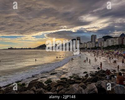 Cumulonimbus-Wolke in dramatisch bewölktem Himmel mit Sonnenstrahlen, die die Menschen am Strand von der Küste der Küste erleuchten. Stockfoto