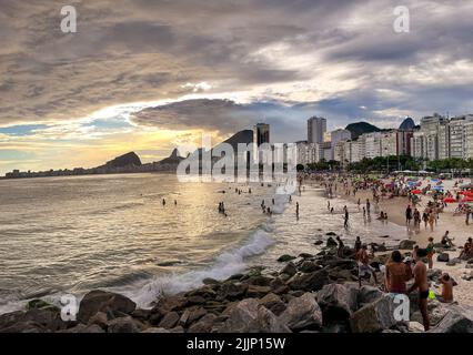 Große Cumulonimbus-Wolke am Horizont in dramatisch bewölktem Himmel und Sonnenstrahlen, die die Menschen am Strand von der Küste von der Küste erleuchten. Stockfoto