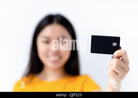 Kreditkarte in weiblichen Händen auf weißem Hintergrund unscharf im Hintergrund glücklich lächelnde asiatische Frau Stockfoto