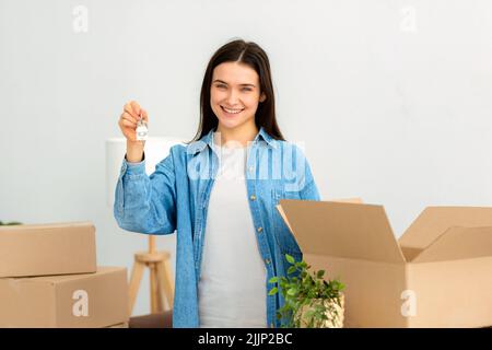 Die junge kaukasische Frau hält die Schlüssel in den Händen, während sie in ihrem neuen Haus steht Stockfoto