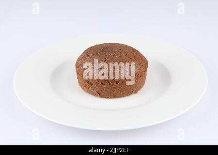 Ein Schokoladensouffle in einem klassischen weißen Porzellan-Ramekin auf einem weißen Teller Stockfoto