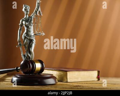 Statuette der Göttin der Gerechtigkeit - Themis, ein hölzerner Gavel eines Richters und ein Buch auf beigem Hintergrund. Symbole eines ehrlichen fairen Prozesses. Constitutio Stockfoto