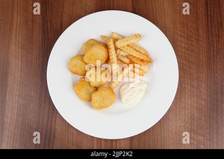 Ein Blick von oben auf weißen Teller mit Nuggets, pommes Frites und Sauce auf einem hölzernen Hintergrund Stockfoto