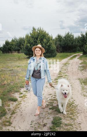 Junge schöne Frau, die mit ihrem weißen Hund samoyed aus der Stadt im Park läuft. Stockfoto