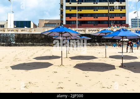 Eine Reihe von blauen Sonnenschirmen mit Schatten auf Sand am Strand Farol da Barra in Salvador, Bahia, Brasilien. Stockfoto