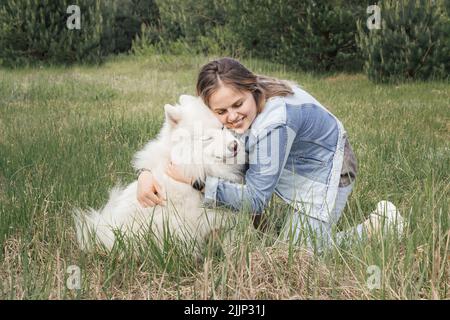 Junge schöne Frau umarmte ihren Hund samoyed, nachdem sie im Park spazieren ging Stockfoto