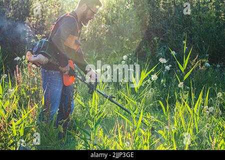 Mann trimmt Unkraut mit Unkrautstrimmer im Sommer Stockfoto