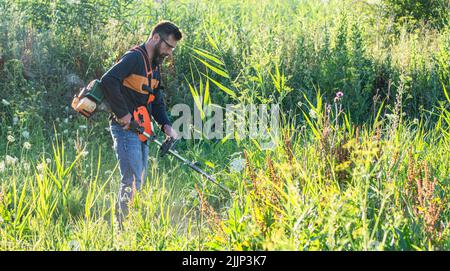 Mann trimmt Unkraut mit Unkrautstrimmer im Sommer Stockfoto