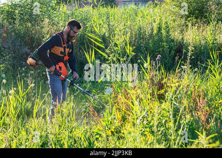 Mann trimmt Unkraut mit Unkrautstrimmer im Sommer Stockfoto