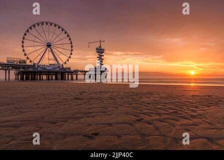 Riesenrad auf einem Pier an einem einsamen Sandstrand bei Sonnenuntergang im Sommer Stockfoto