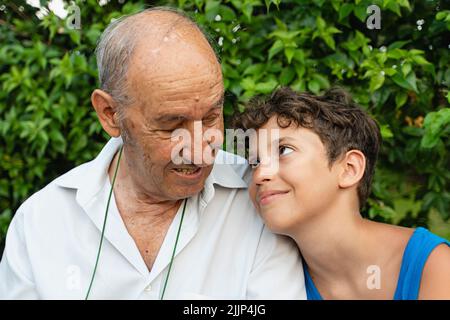 Großvater und EnkelGroßvater und Enkel tauschen liebevolle Blicke aus, die draußen sitzen - multigenerationales Familienmenschen-Lifestyle-Konzept Stockfoto