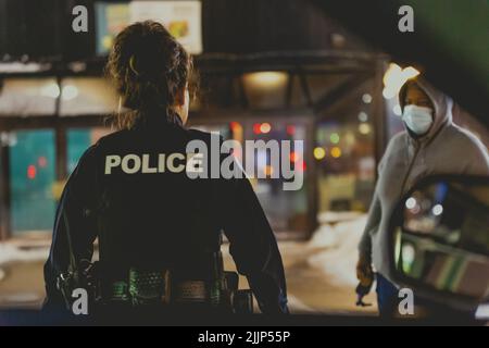 Eine Polizistin, die sich einem Zeugen einer örtlichen Störung nähert, ruft nachts auf der Straße an Stockfoto