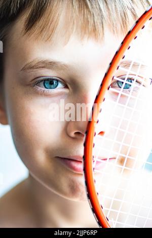 Junge, der einen Tennisschläger vor seinem Gesicht hält Stockfoto