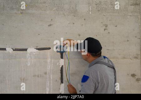 Bild eines Elektrikers, der eine Elektrosonde durch ein Wellrohr auf der Baustelle führt. Realisierung eines elektrischen Systems Stockfoto