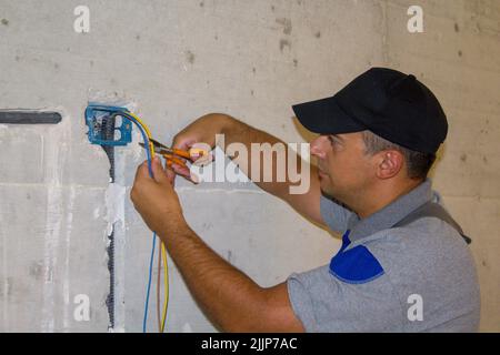 Bild eines Elektrikers, der mit einer Schere Stromkabel schneidet. Die Realisierung des elektrischen Systems des Hauses. Stockfoto