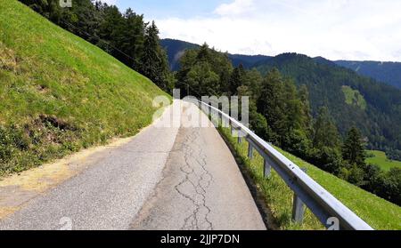 Die Straße, die durch das Dorf mit hohen Hügeln mit dichten Bäumen an einem sonnigen Tag bedeckt Stockfoto