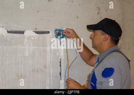 Bild eines Elektrikers, der eine elektrische Sonde durch ein Corugatrohr auf der Baustelle führt. Realisierung eines elektrischen Systems von einem h Stockfoto