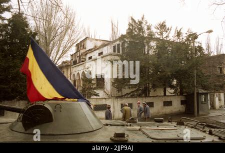 Bukarest, Rumänien, Januar 1990. Pangratti Straße, in der Nähe des Hauptquartiers des öffentlichen rumänischen Fernsehsenders. Ein Armeepanzer vor einem Gebäude, das während der antikommunistischen Revolution im Dezember 1989 durch den Schusswechsel beschädigt wurde. Stockfoto