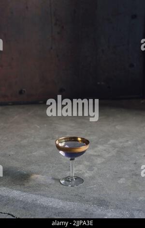 Klassischer Cocktail aus Arsen und alter Spitze, lila und goldener Drink aus Coupé-Glas auf Beton Stockfoto