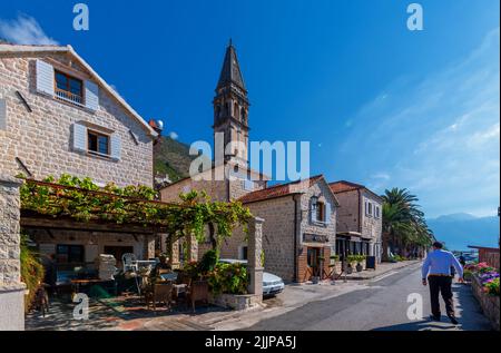 Der Glockenturm der Nikolaikirche in Perast, Montenegro, und eine Person, die an einem sonnigen Tag vorbei geht Stockfoto