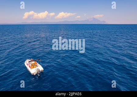 Weißes Segelboot, das sich in Richtung Mt Athos bahnt. Ruhiges Meer. Schöner Himmel mit flauschigen Wolken. Luftdrohnenansicht. Hochwertige Fotos Stockfoto