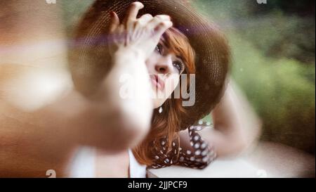 Ein Porträt einer attraktiven deutschen Frau, die ihren Pony in einem Sommerstrohhut fixiert Stockfoto