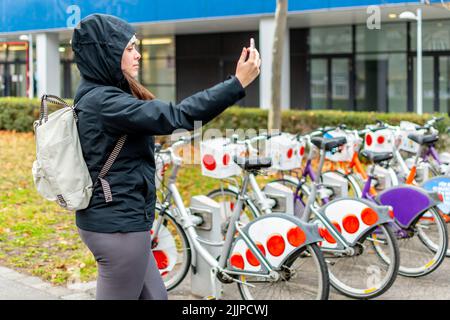 Nahaufnahme einer jungen Frau in der Nähe einer Fahrradverleihstation auf einem öffentlichen Parkplatz in der Stadt Stockfoto