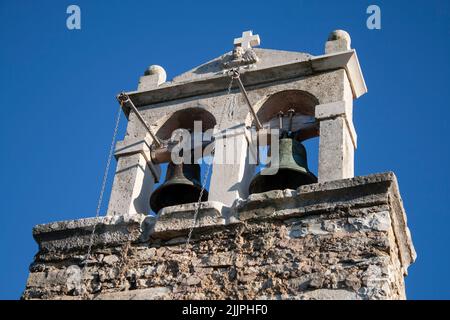 Ein niedriger Winkel von einem Steinkreuz und zwei Glocken einer alten Kirche gegen den blauen Himmel in hellem Sonnenlicht Stockfoto