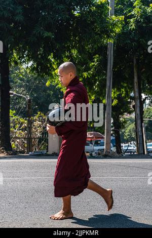 Eine vertikale Aufnahme eines Mönchs in roten Gewändern geht die Straße in Yangon Myanm hinunter Stockfoto