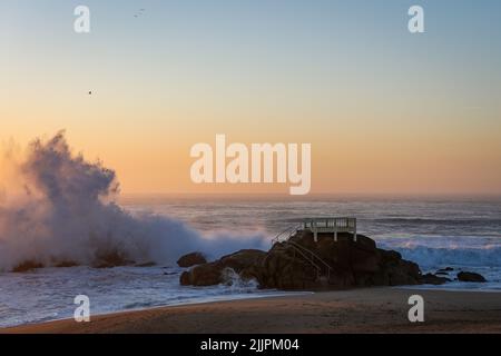 Die Wellen schlagen die großen Felsen an der Küste vor dem Hintergrund des Sonnenuntergangs Stockfoto