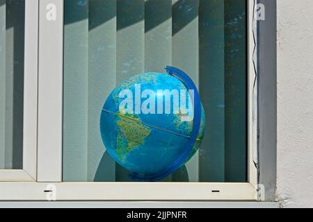 Blauer Globus im Fenster mit weißen Jalousie aka Jalousien, moderner Bildungsvielfalt Stockfoto