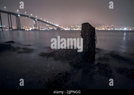 Eine wunderschöne Nachtaufnahme einer Brücke und einer Stadt, die sich im Winter in Tromso, Norwegen, im Wasser spiegelte Stockfoto