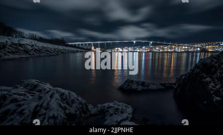 Eine wunderschöne Nachtaufnahme einer Brücke und einer Stadt, die sich im Winter in Tromso, Norwegen, im Wasser spiegelte Stockfoto