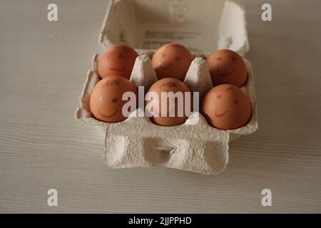 Eine Nahaufnahme von Eiern mit gemalten Emotionen in einem Eierkarton Stockfoto