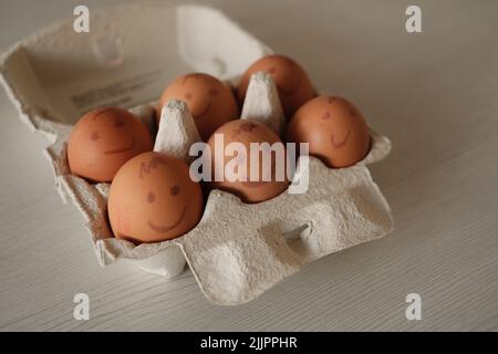 Eine Nahaufnahme von Eiern mit gemalten Emotionen in einem Eierkarton Stockfoto