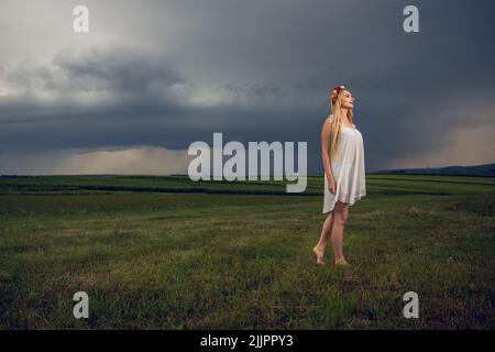 Nahaufnahme eines kaukasischen blonden Weibchens, das auf einem grünen Feld unter einem bewölkten Himmel steht Stockfoto