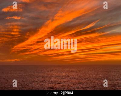 Ein hypnotisierender, orangefarbener, wolkig gebetter Sonnenuntergang über einem ruhigen Meer Stockfoto