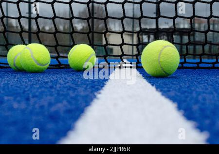 Das Netz eines blauen Paddle-Tennisplatzes und vier Kugeln in der Nähe der weißen Linie Stockfoto
