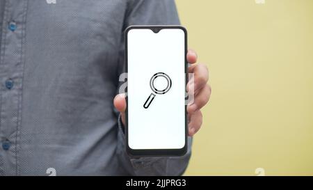 Eine Nahaufnahme eines Mannes, der ein Telefon hält, mit einer 2D-Abbildung eines Suchsymbols darauf Stockfoto
