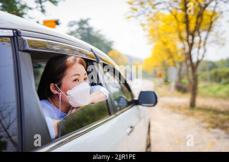 Eine wunderschöne südostasiatische Frau in einer Gesichtsmaske, die aus dem Autofenster schaut Stockfoto