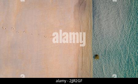 Eine Luftaufnahme von einer Reihe von Fußabdrücken am Sandstrand, der zur Küste führt Stockfoto