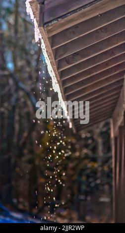 Eine vertikale Wassertropfen, die vom Dach eines Holzgebäudes herabfließen Stockfoto