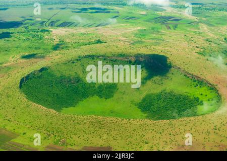 Vogelperspektive auf grün bewachsenen Krater in der Serengeti, umgeben von lokalen Dörfern, Arusha, Tansania Stockfoto