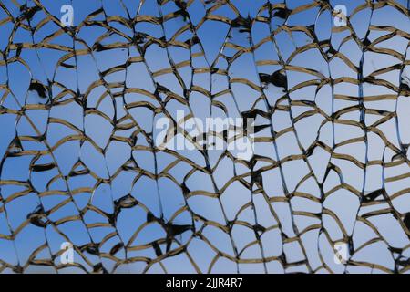 Wunderschöne silberne Linien eines zerschmetterten Fensters erzeugen ein komplexes Muster vor einem tiefblauen Himmel. Stockfoto
