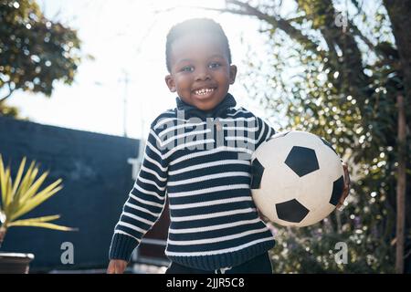 Ein entzückender kleiner Junge, der draußen mit seinem Ball spielt. Stockfoto