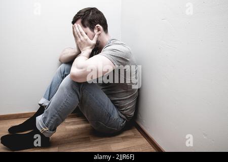 Ein trauriges Männchen mit den Händen auf dem Gesicht in der Ecke Stockfoto